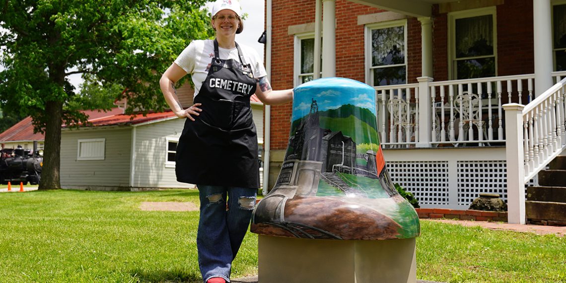 An artist poses beside Greene County's "Coal & Country" painted bell outside the Greene County Historical Society Museum in Waynesburg.