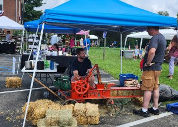 A vintage hay baler demonstration takes place among vendor booths during the Old Glory in Greene County Festival at Bootsie's Bed & Breakfast.