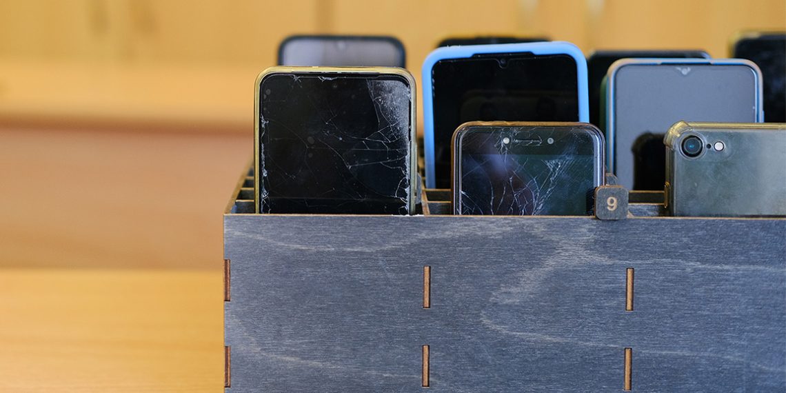 Several smartphones are stored in a wooden classroom organizer used to hold student devices during the school day.