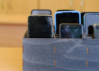 Several smartphones are stored in a wooden classroom organizer used to hold student devices during the school day.