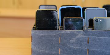 Several smartphones are stored in a wooden classroom organizer used to hold student devices during the school day.