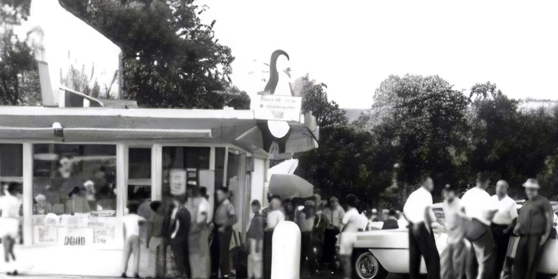 A vintage black and white photo shows customers lined up outside a busy Dari Delite ice cream stand with classic cars parked nearby.