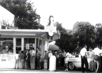 A vintage black and white photo shows customers lined up outside a busy Dari Delite ice cream stand with classic cars parked nearby.