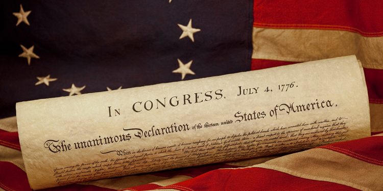 A rolled copy of the Declaration of Independence rests on an American flag with the date July 4, 1776, visible at the top.