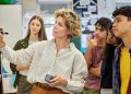 A teacher writes on a whiteboard while several high school students watch during a classroom lesson.