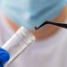 A healthcare professional uses tweezers to place a tick into a specimen container while wearing protective gloves.