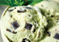 Close up of mint chocolate chip ice cream with large dark chocolate chunks in creamy pale green scoops.