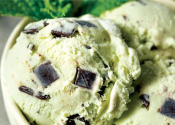 Close up of mint chocolate chip ice cream with large dark chocolate chunks in creamy pale green scoops.