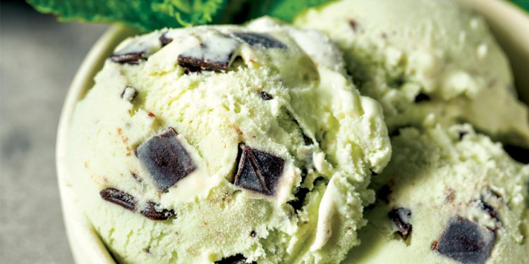 Close up of mint chocolate chip ice cream with large dark chocolate chunks in creamy pale green scoops.