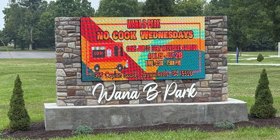 A stone entrance sign at Wana B Park displays a digital message promoting the park's "No Cook Wednesdays" event.