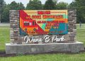 A stone entrance sign at Wana B Park displays a digital message promoting the park's "No Cook Wednesdays" event.