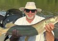 An angler proudly holds a large muskellunge in a fishing boat after landing the trophy fish.