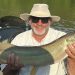 An angler proudly holds a large muskellunge in a fishing boat after landing the trophy fish.
