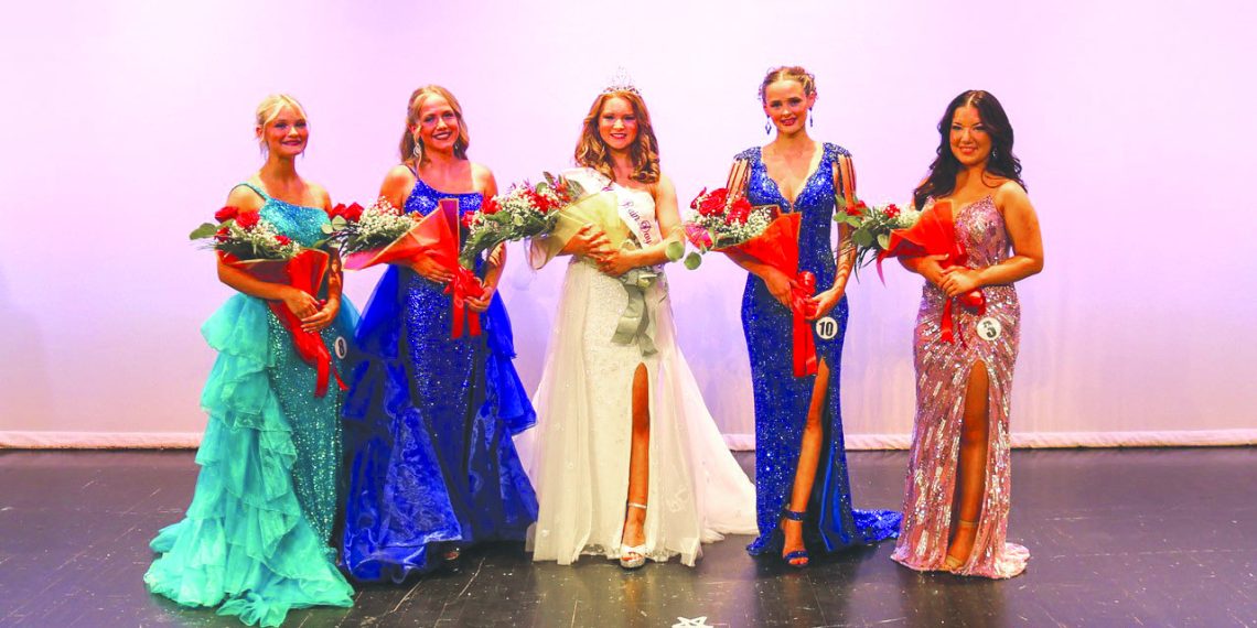 Five women in formal gowns pose on a stage, with the crowned woman in the center holding a bouquet and surrounded by four other women holding flowers.
