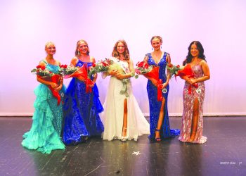 Five women in formal gowns pose on a stage, with the crowned woman in the center holding a bouquet and surrounded by four other women holding flowers.
