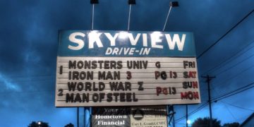 A vintage Sky View Drive-In marquee lists Monsters University, Iron Man 3, World War Z, and Man of Steel beneath a dark stormy evening sky.