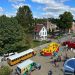 Aerial view of families enjoying a community event with an inflatable obstacle course, school bus, food truck, and emergency vehicles.