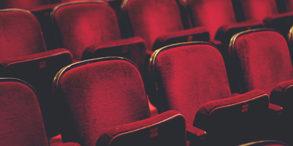 Empty red theater seats arranged in rows under dim lighting.