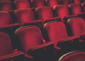 Empty red theater seats arranged in rows under dim lighting.