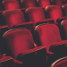 Empty red theater seats arranged in rows under dim lighting.