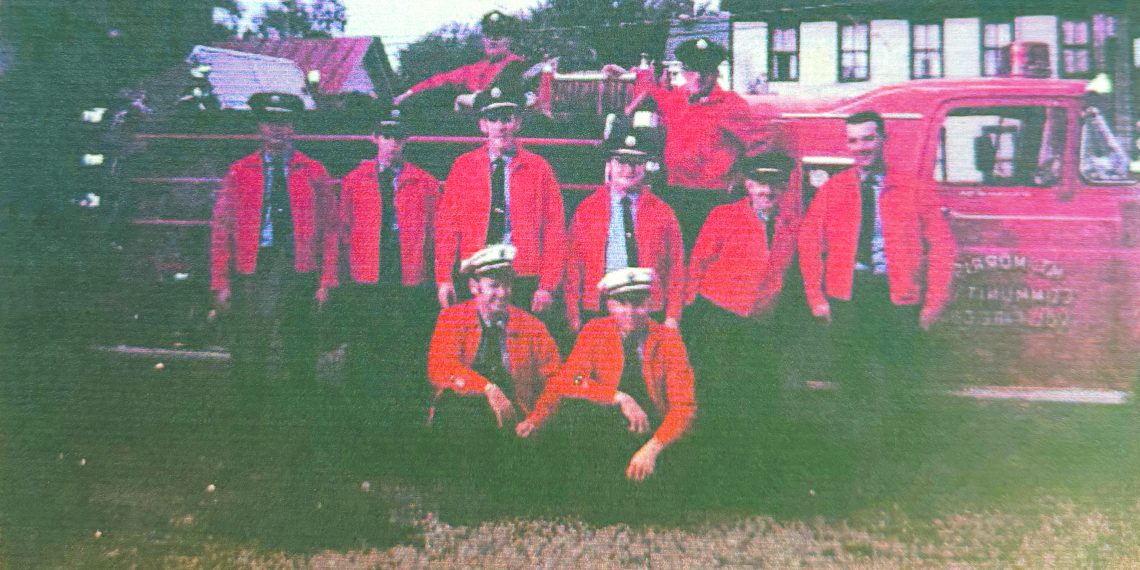 A group of Mount Morris volunteer firefighters poses beside a vintage red fire truck.