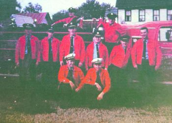 A group of Mount Morris volunteer firefighters poses beside a vintage red fire truck.