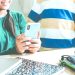 Two students in a classroom with one student holding a smartphone at a table with school supplies.