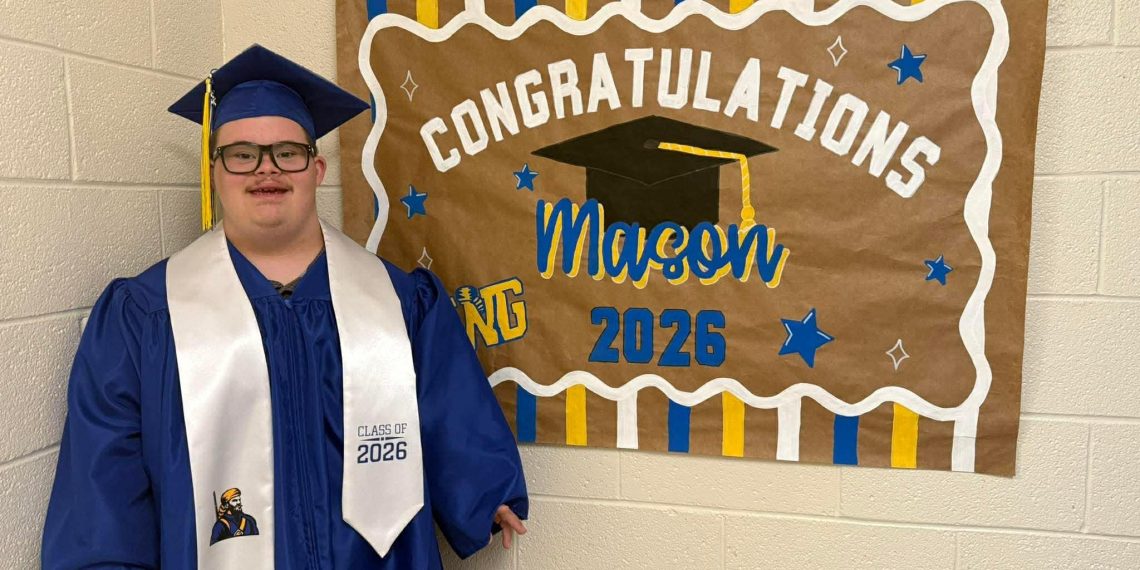 Mason smiles in a blue graduation cap and gown beside a handmade “Congratulations Mason” Class of 2026 sign.