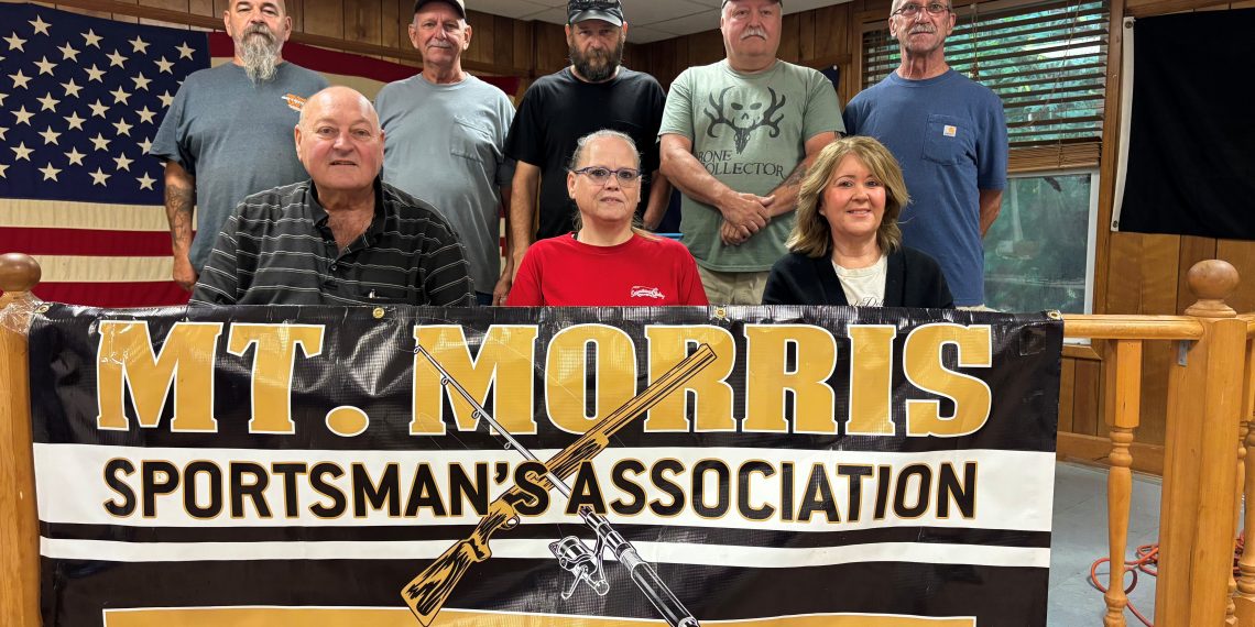 Members of the Mount Morris Sportsman’s Association pose behind a banner celebrating the club’s 75th anniversary.