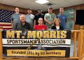 Members of the Mount Morris Sportsman’s Association pose behind a banner celebrating the club’s 75th anniversary.