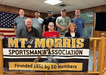 Members of the Mount Morris Sportsman’s Association pose behind a banner celebrating the club’s 75th anniversary.
