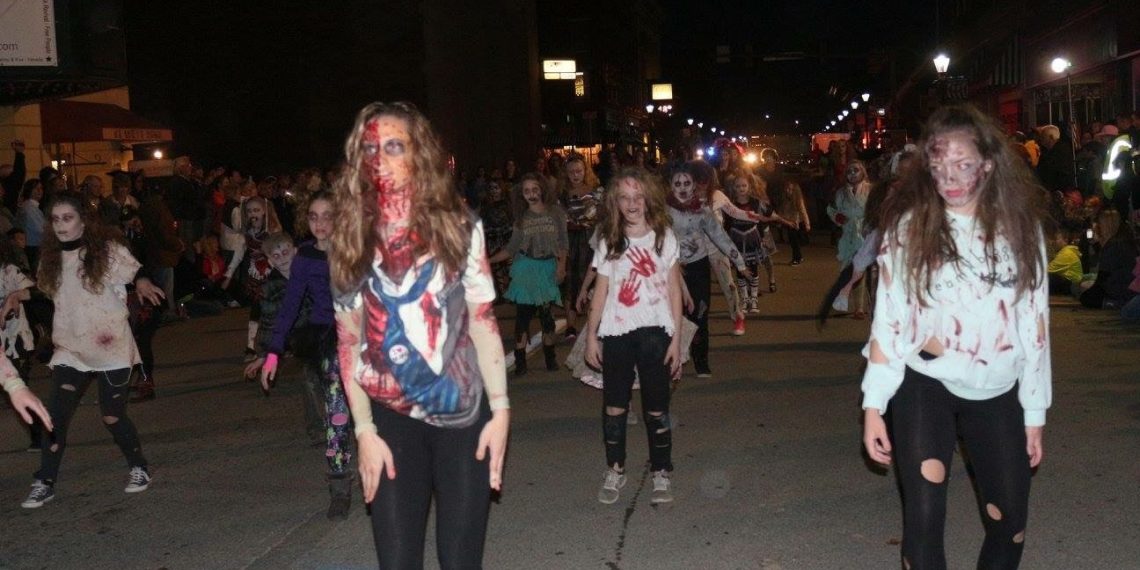 A large group of people dressed as zombies performs a Thriller-inspired dance on a downtown street at night.