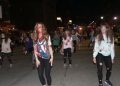 A large group of people dressed as zombies performs a Thriller-inspired dance on a downtown street at night.