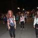 A large group of people dressed as zombies performs a Thriller-inspired dance on a downtown street at night.
