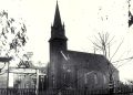 Historic black-and-white photograph of a Gothic church and downtown Waynesburg buildings, with a “Monongahela Whiskey” sign visible in the foreground.