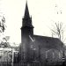 Historic black-and-white photograph of a Gothic church and downtown Waynesburg buildings, with a “Monongahela Whiskey” sign visible in the foreground.