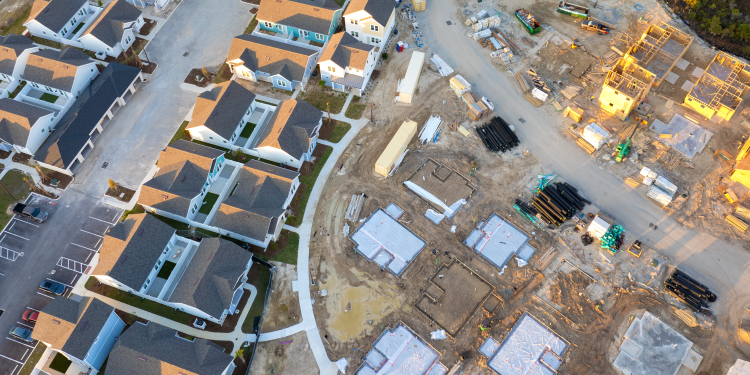 Aerial view of a residential neighborhood with completed homes beside an active construction site with foundations, building materials, and heavy equipment.