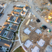 Aerial view of a residential neighborhood with completed homes beside an active construction site with foundations, building materials, and heavy equipment.
