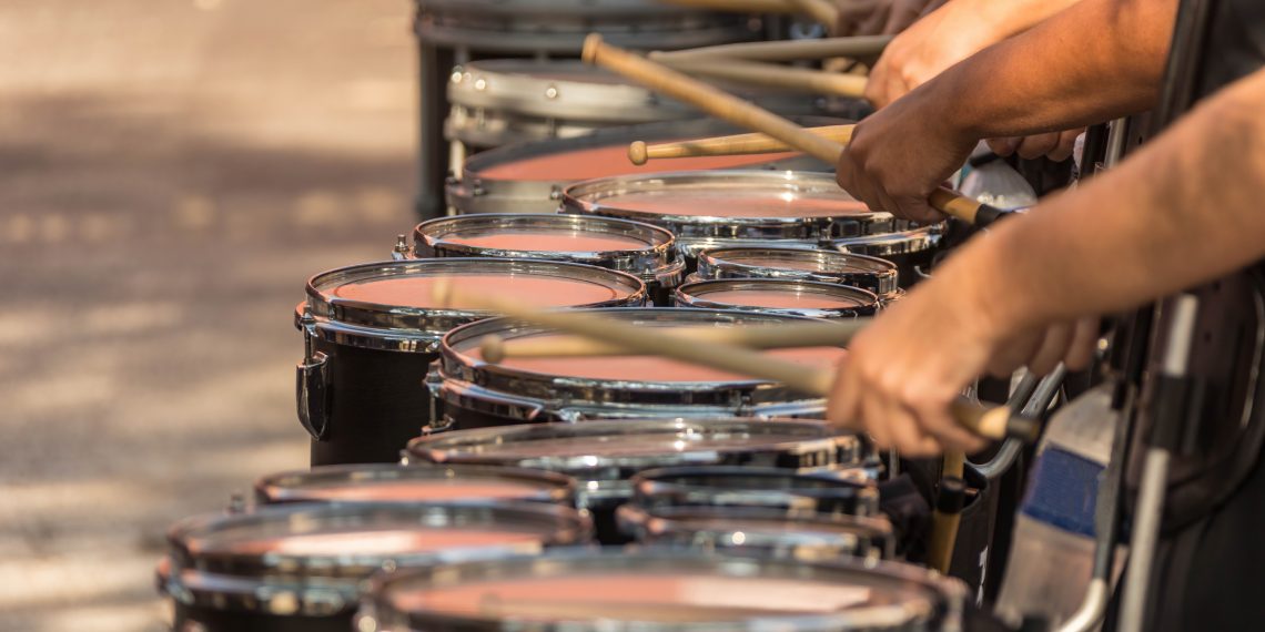 Marching band drummers play a row of drums during a performance.