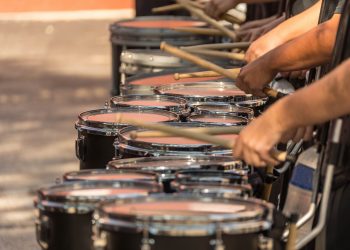 Marching band drummers play a row of drums during a performance.