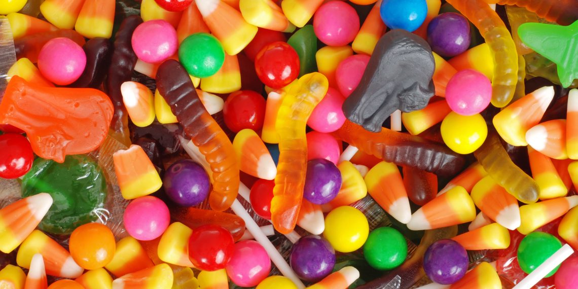 An assortment of colorful Halloween candies, including candy corn, gummy worms, lollipops, and round fruit-flavored candies.