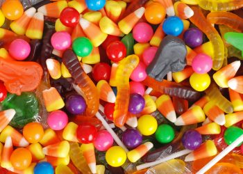 An assortment of colorful Halloween candies, including candy corn, gummy worms, lollipops, and round fruit-flavored candies.