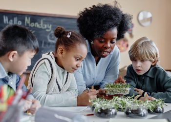 A teacher helps three young students examine seedlings during a hands-on classroom activity.