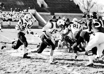A vintage black-and-white photograph shows Waynesburg College football players in white uniforms running the ball against opposing defenders during a 1960s football game.