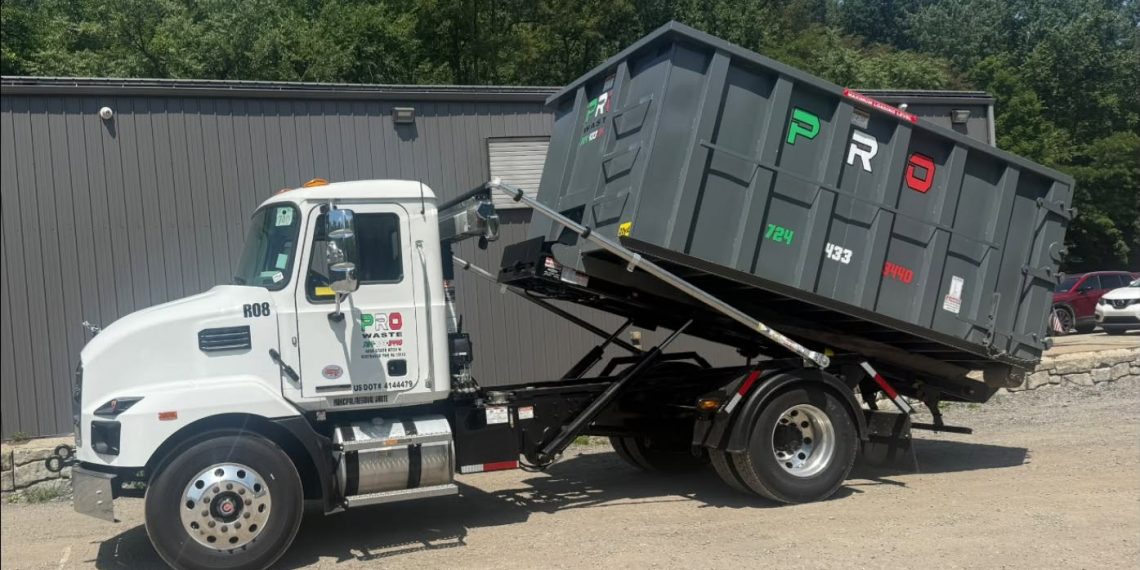 A white Pro Waste LLC truck with a raised gray roll-off dumpster is parked outside a commercial building in southwestern Pennsylvania.