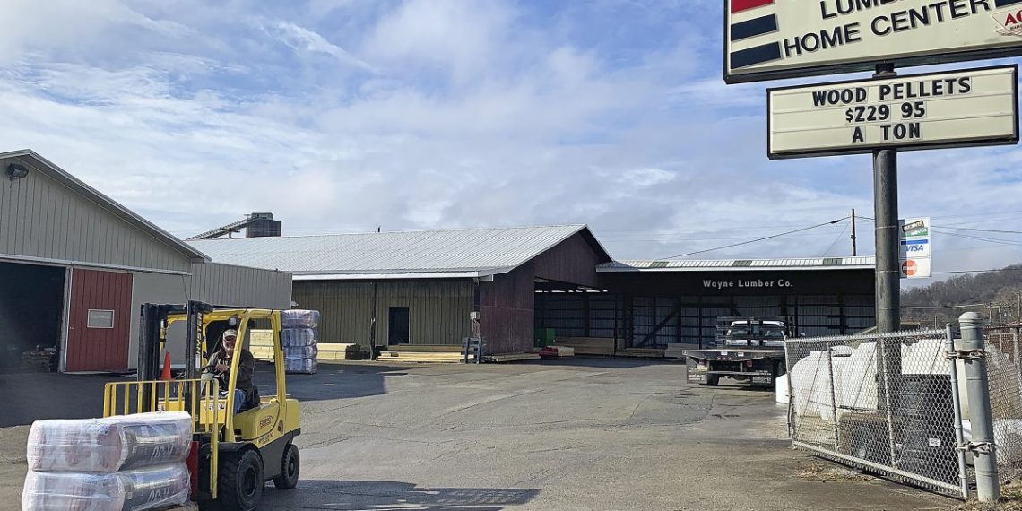 A forklift transports building materials outside Wayne Lumber & Supply in Waynesburg, Pennsylvania, with lumberyard buildings and a large Wayne Lumber Home Center sign visible.