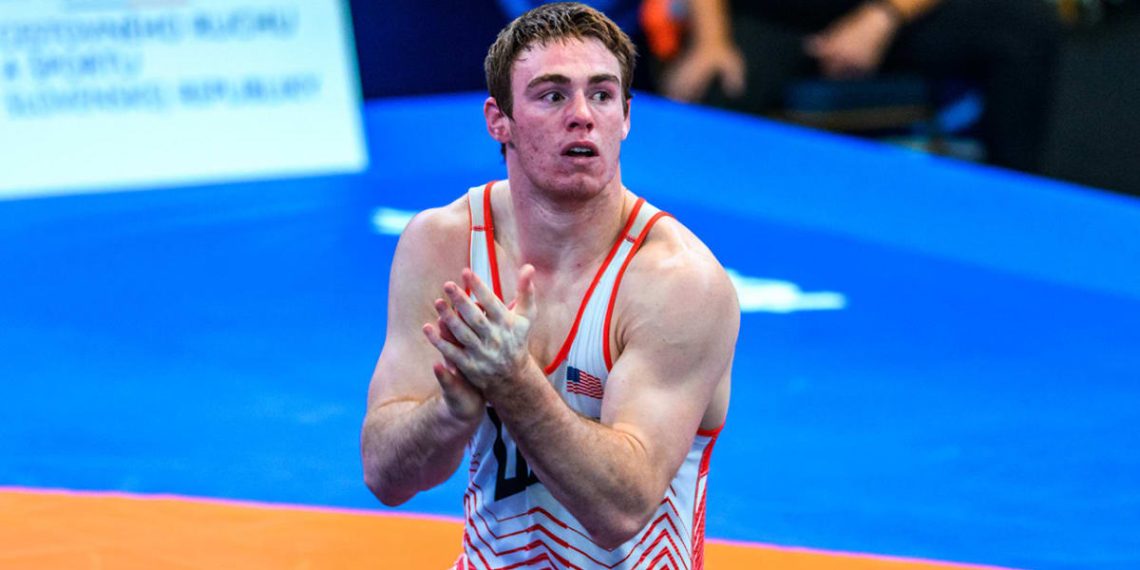 U20 World Wrestling Champion Michael Boyle claps his hands while wearing a red and white USA wrestling singlet on a competition mat.