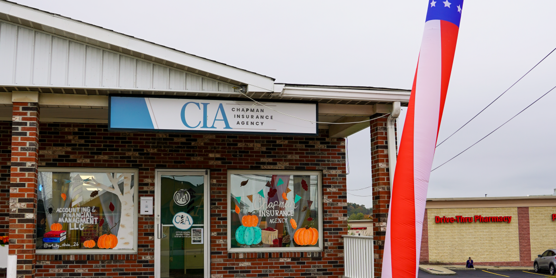 Chapman Insurance Agency's new Waynesburg office features autumn window decorations, a storefront sign, and a tall patriotic inflatable waving figure outside the entrance.