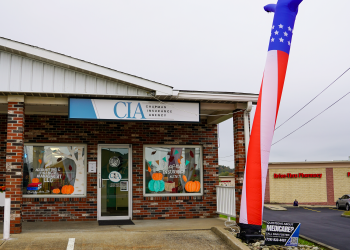 Chapman Insurance Agency's new Waynesburg office features autumn window decorations, a storefront sign, and a tall patriotic inflatable waving figure outside the entrance.