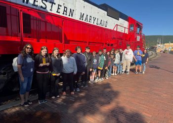 Carmichaels students and a teacher stand beside a red and white Western Maryland Railway locomotive during a fall field trip aboard the Frostburg Flyer.